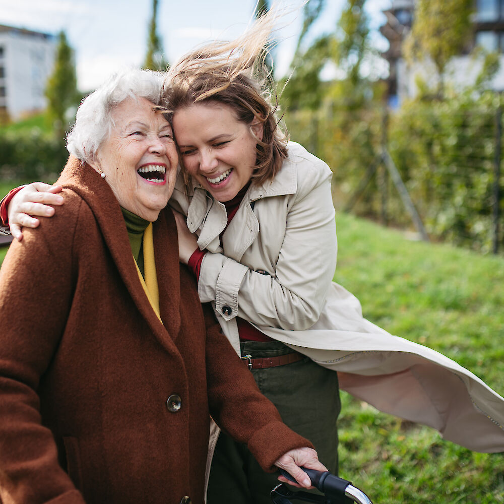 Eine Frau umarmt ihre Mutter, sie lachen herzlich.